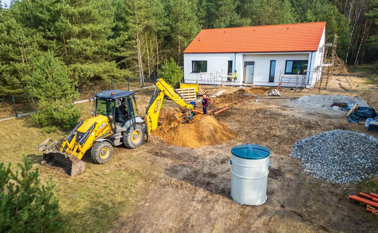 Montaż przydomowej biologicznej oczyszczalni ścieków EkoHouse przy domu jednorodzinnym – koparka przygotowująca wykop pod zbiornik oczyszczalni